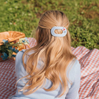 Woman wearing a light blue patterned flat round hair clip in long blonde wavy hair during outdoor picnic.