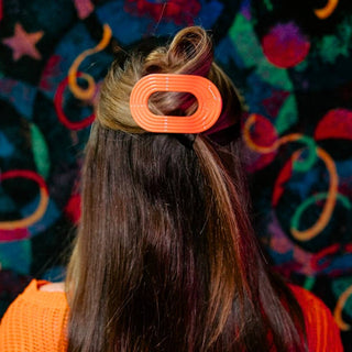 Woman wearing orange oval-shaped hair clip in brunette hair against colorful patterned background.