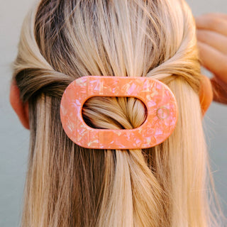 Woman wearing a coral-colored flat round hair clip in blonde hair styled in half-up ponytail