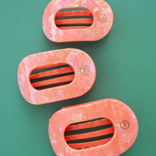Three oval-shaped hair clips with translucent coral frames and black-striped centers on green background
