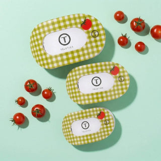 Three TELETIES flat round hair clips with green gingham pattern surrounded by fresh cherry tomatoes on mint background.