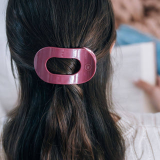 Woman wearing a pink oval-shaped hair clip holding back dark brown wavy hair