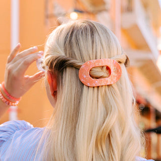 Woman wearing orange flat round hair clip in blonde hair, adjusting hairstyle with hand