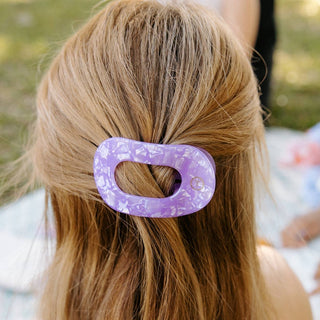 Woman wearing a purple marbled flat round hair clip holding back blonde hair in casual style.