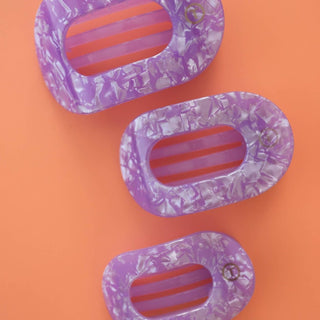 Three oval-shaped flat hair clips with purple marble pattern and striped centers on orange background