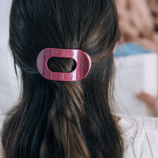 Woman wearing pink flat round hair clip in dark brown hair, viewed from behind.