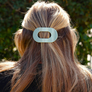 Woman wearing a small translucent oval hair clip holding back blonde highlighted hair in half-up style.