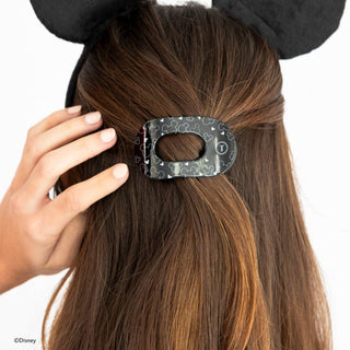 Woman wearing Disney Mickey Mouse ears touching a black Disney-themed hair clip in her brown hair.
