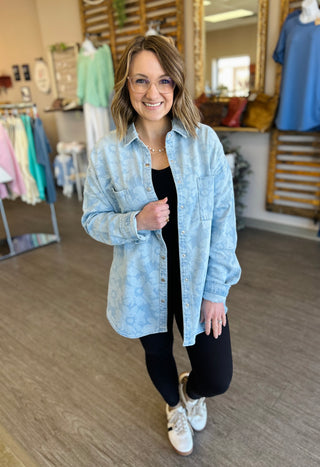Woman wearing light blue floral denim shacket over black outfit in clothing boutique store setting