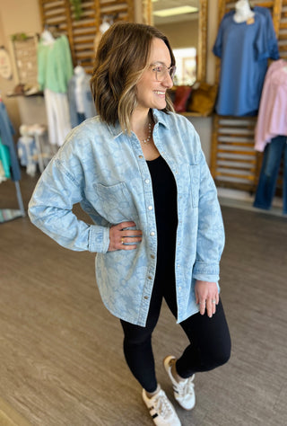 Woman wearing oversized light blue denim shacket over black outfit in clothing store setting.