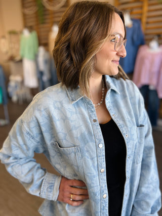 Woman wearing light blue denim button-up shirt jacket over black top in casual indoor setting