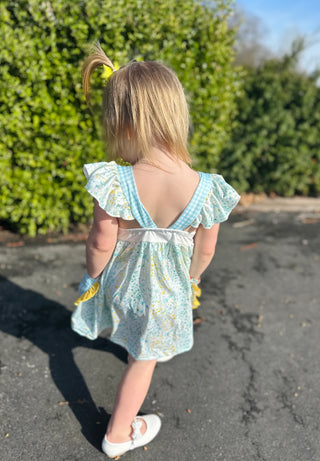 Young girl wearing floral dress with ruffled sleeves and open back detail, walking outdoors.