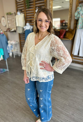 Woman wearing cream lace tie-front blouse with embroidered jeans in clothing boutique setting