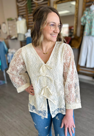 Woman wearing cream floral lace tie-front blouse with jeans in clothing store setting