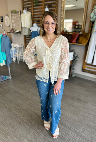 Woman wearing cream lace tie-front blouse with embroidered jeans in clothing boutique setting