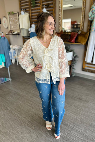 Woman wearing white floral lace tie-front blouse with jeans in clothing boutique store setting.