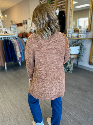 Woman wearing textured knit cardigan and jeans standing in retail store, shown from behind