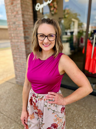 Woman wearing fuchsia sleeveless bodysuit with floral skirt and glasses, smiling outdoors