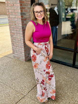 Woman wearing bright pink sleeveless bodysuit with floral wide-leg pants, standing outdoors smiling