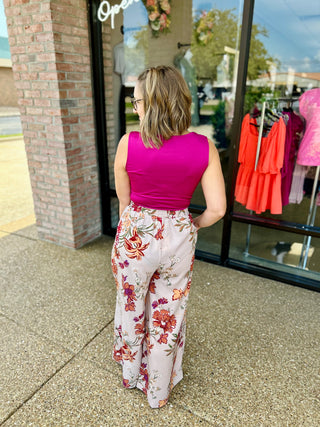Woman wearing fuchsia sleeveless bodysuit with floral pants standing outside boutique storefront