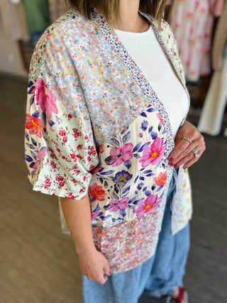 Woman wearing colorful floral patchwork kimono over white top and jeans in boutique setting