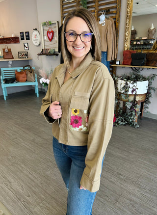 Woman wearing beige denim jacket with floral embroidered pocket detail in boutique setting