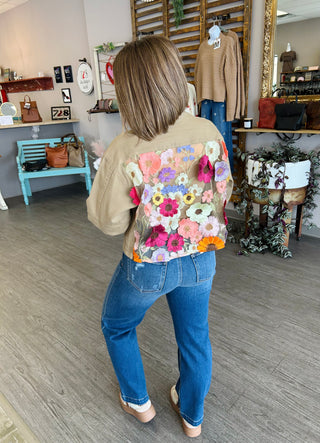 Woman wearing floral embroidered denim jacket with jeans in boutique clothing store