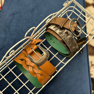 Two genuine leather belts with decorative buckles displayed in a wire basket on blue surface.