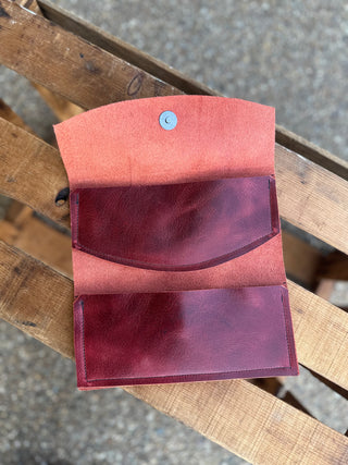 Open handcrafted leather wallet showing interior compartments and magnetic closure, displayed on wooden surface.