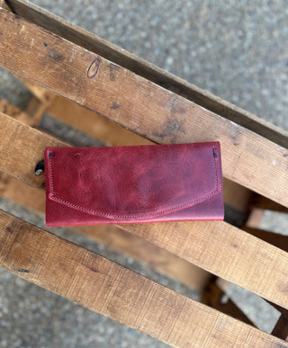 Red leather wallet with envelope flap closure sitting on weathered wooden crate slats outdoors.