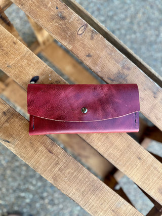 Handcrafted leather wallet with snap closure displayed on rustic wooden slats outdoors