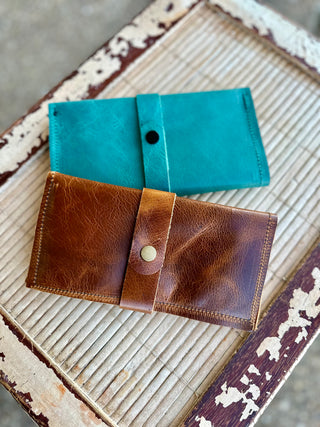 Two leather wrap wallets in different colors displayed on rustic wooden surface with weathered paint
