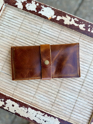 Brown leather wrap wallet with snap closure and visible stitching on weathered wooden surface.