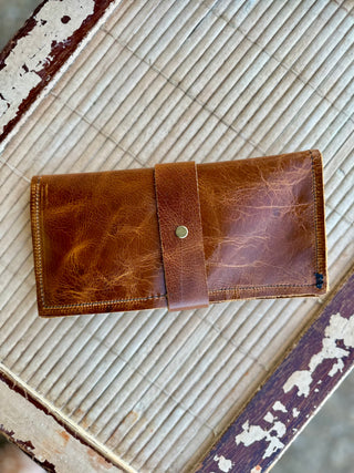 Brown leather wrap wallet with snap closure displayed on rustic bamboo mat surface