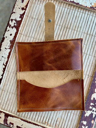 Handcrafted brown leather wrap wallet with tan accent strip and snap closure on rustic wooden surface.