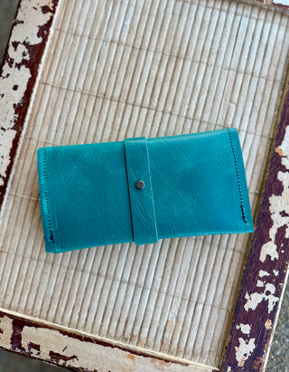 Turquoise leather wrap wallet with snap closure displayed on vintage textured surface