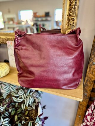 Burgundy leather tote bag displayed on wooden shelf with ornate gold mirror frame in background.