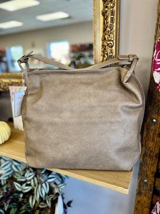 Tan leather tote bag with shoulder straps displayed on wooden shelf in retail store setting.