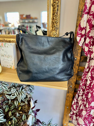 Black leather tote bag with handles displayed on wooden shelf in boutique setting