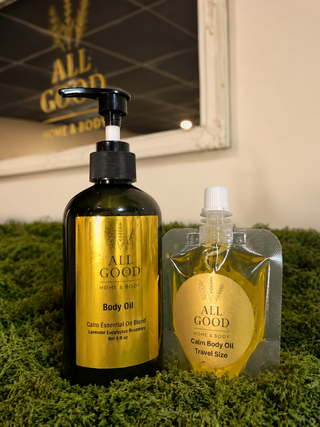 All Good Home & Body Calm Body Oil full size pump bottle and travel size pouch displayed on moss.