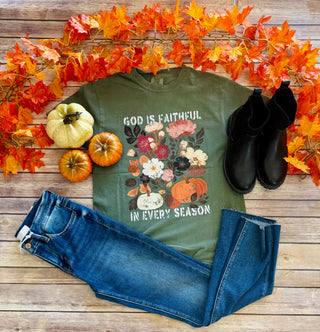 Fall-themed t-shirt with pumpkins and flowers displayed with jeans, boots, and autumn decorations on wooden background.