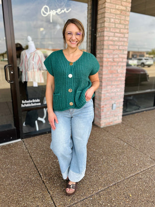 Woman wearing a knit button-down sweater top with gold buttons and front pockets.