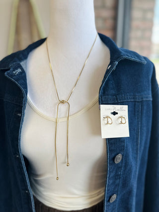 Gold lariat-style necklace displayed on mannequin wearing denim jacket and cream top.