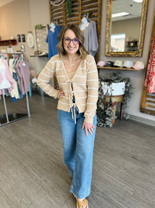 Woman wearing striped tie-front cardigan with jeans in boutique clothing store setting