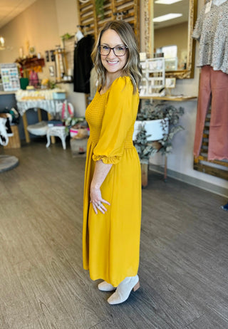 Woman wearing yellow smocked midi dress with three-quarter sleeves in boutique setting