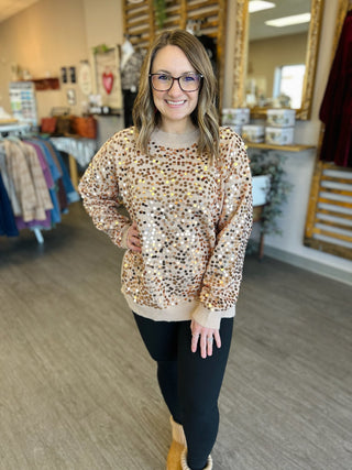 Woman wearing golden sequin sweater with dark jeans standing in clothing boutique store
