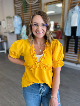 Woman wearing bright yellow ruffle top with puffed sleeves and jeans in clothing store setting
