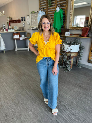 Woman wearing yellow ruffle top with jeans standing in clothing boutique store interior