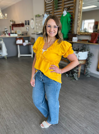 Woman wearing bright yellow ruffle top with jeans standing in boutique clothing store