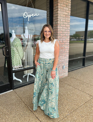 Woman wearing flowy wide-leg palazzo pants with paisley print, paired with white sleeveless top.